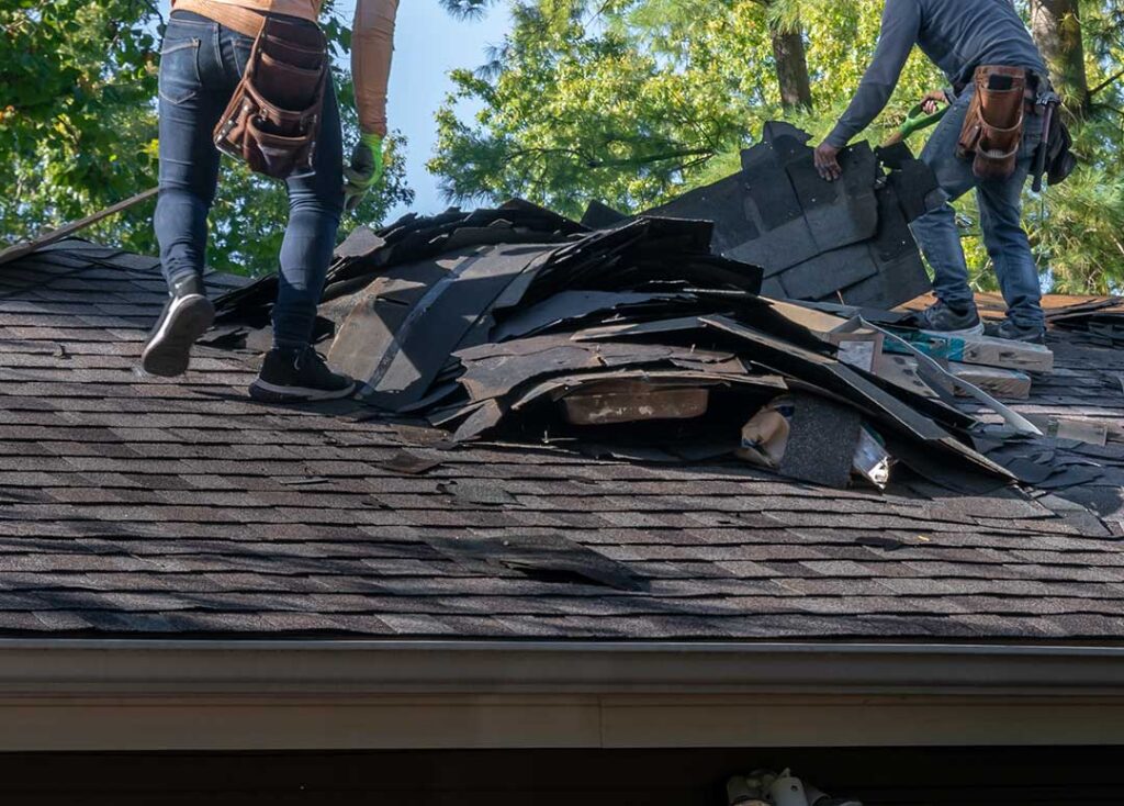 Homeowner comparing asphalt shingles, metal panels, and slate samples beside a residential roof.
